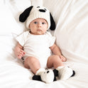 A sitting baby wearing a Snoopy beanie with flappy ears, and matching Snoopy baby booties, a knitting kit from Stitch & Story made with 100% merino wool.