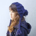 A woman is wearing a newly knitted Cable Coo Hat in Midnight Blue, made from Stitch & Story's knitting kit.