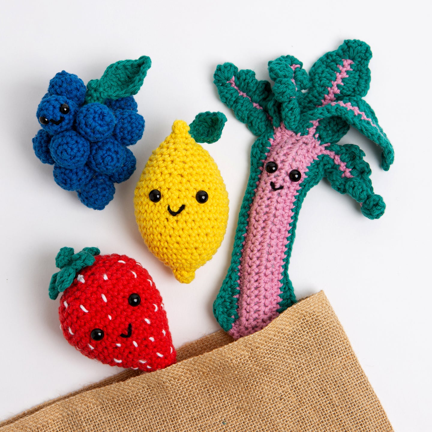 4 smiling fruits - Aubrey the Strawberry, Merlot the Grape, Lemmy the Lemon and Bard the Rhubarb are cheekily escaping from a jute bag.