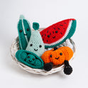 5 Fruit crochet amigurumi toys are all placed in a small basket with their smiling faces facing outwards. They include Perry the Pear in Pale Blue Cotton One, Penelope Pea in a Pod in Forest Green Cotton One, Melany the Watermelon in Red Apple Cotton One, Paul the Pumpkin in Deep Orange Cotton One and Courtney the Courgette in Forest Green Cotton One.