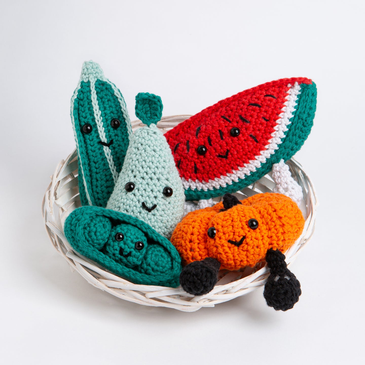 5 Fruit crochet amigurumi toys are all placed in a small basket with their smiling faces facing outwards. They include Perry the Pear in Pale Blue Cotton One, Penelope Pea in a Pod in Forest Green Cotton One, Melany the Watermelon in Red Apple Cotton One, Paul the Pumpkin in Deep Orange Cotton One and Courtney the Courgette in Forest Green Cotton One.