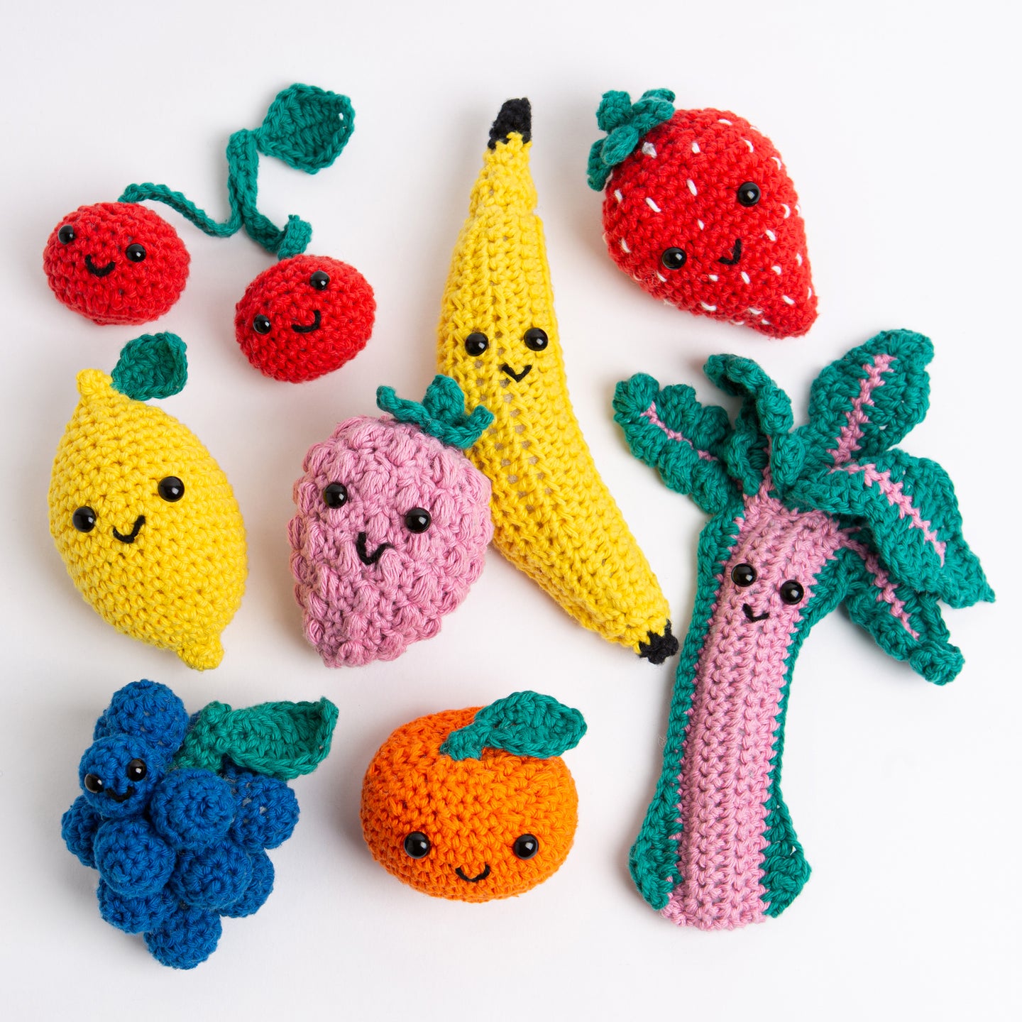 8 fruit crochet amigurumi toys are laid out on a white background with all their smiling faces looking at the camera.