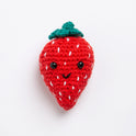 A strawberry toy made with Stitch & Story Cotton One in Red Apple has a joyful smiley face, with white seed sewn all around its red body, with a Forest Green stalk at the top, on a white background