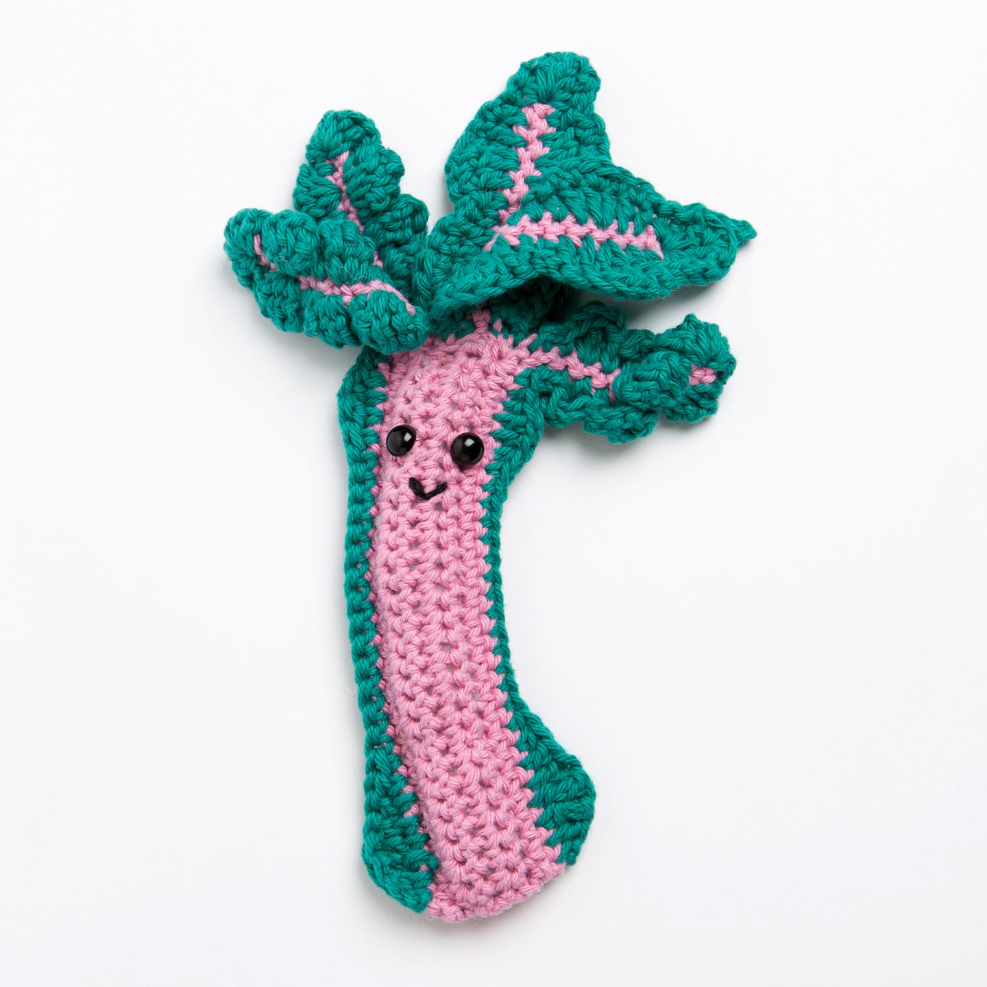 A rhubarb toy made with Stitch & Story Cotton One in Rose Pink has a joyful smiley face, with a Forest Green trimming around and leaves at the top, on a white background