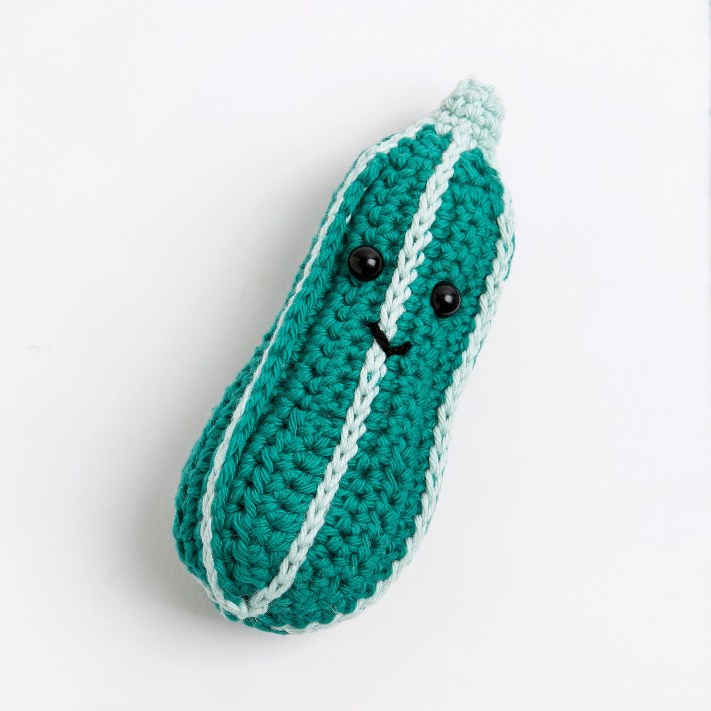 A courgette toy made with Stitch & Story Cotton One in Forest Green has a joyful smiley faces, with segment lined by Pale Blue colour, on a white background