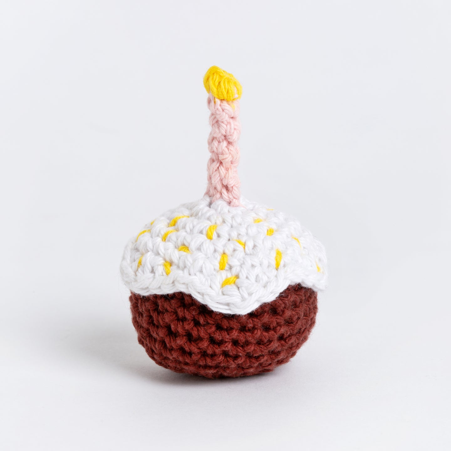 A front on photo to show the candle-lit sugar glazed crochet cupcake in brown.