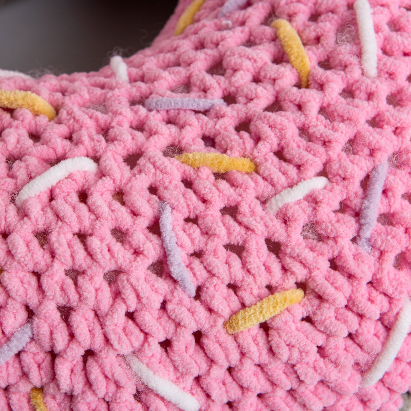 A close up of the pink doughnut sprinkled with Yellow, lilac and white lines, crocheted in Stitch & Story's Roly Poly Plush.
