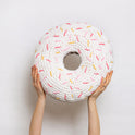 Someone is holding high up a giant round ring white glazed plush cushion with light pink, dark pink and yellow sprinkles, all made with Stitch & Story Roly Poly Plush. 