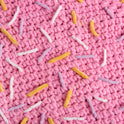 A close up of the pink doughnut blanket, showing all the lilac, yellow and white sprinkles. All crocheted and stitched with Stitch & Story's Roly Poly Plush.
