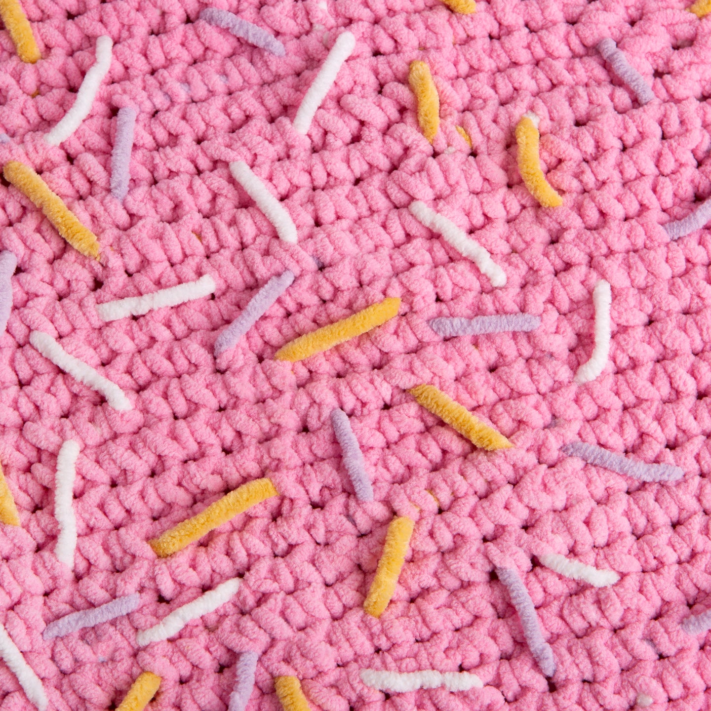 A close up of the pink doughnut blanket, showing all the lilac, yellow and white sprinkles. All crocheted and stitched with Stitch & Story's Roly Poly Plush.