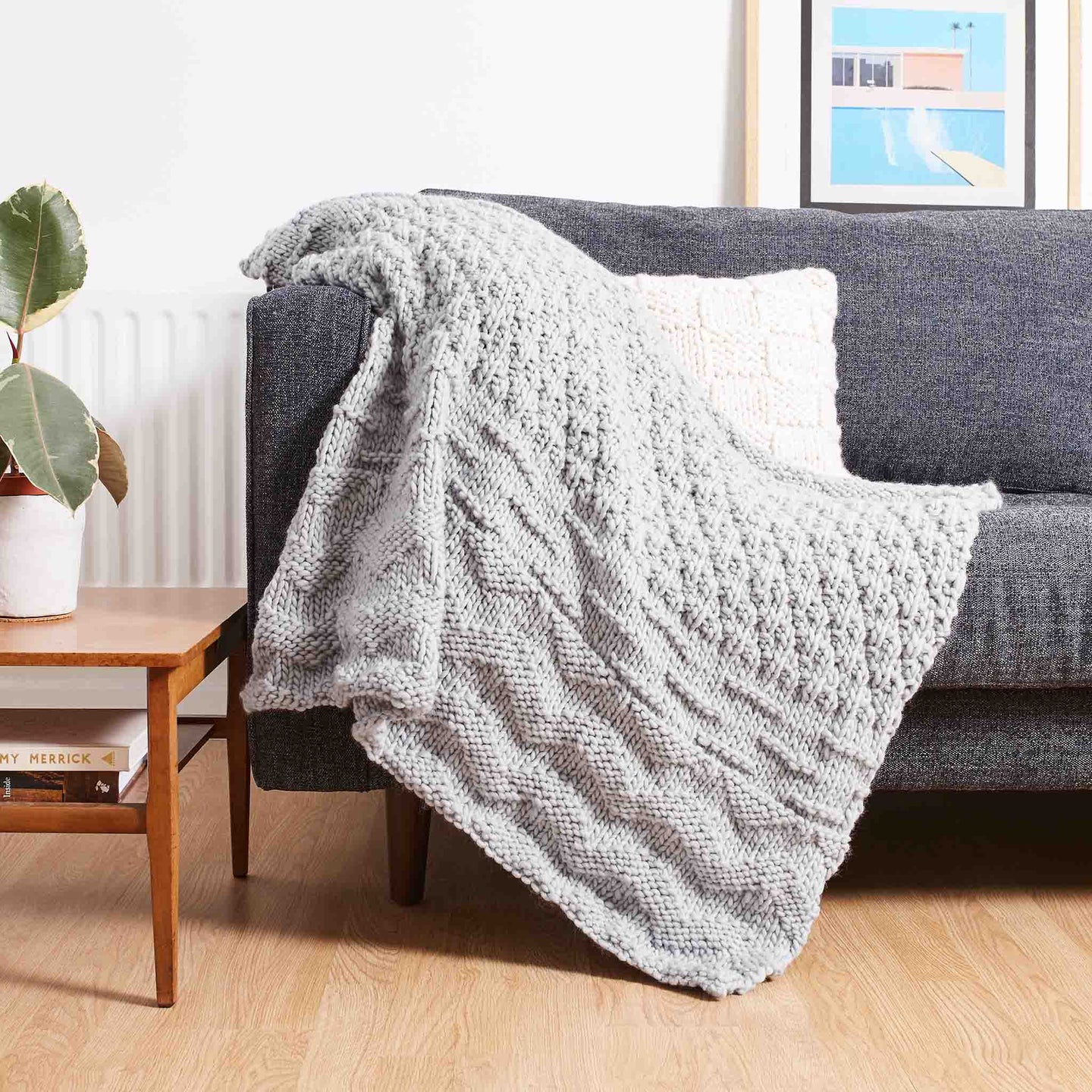 Stitch & Story's soft Lofty Throw knitted in 100% Merino wool Chunky wool in Stormy Grey on a sofa.