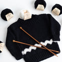 Photo of the Charlie Brown kid sweater, knitted from the knitting kit by Stitch & Story. The long-sleeve sweater is in Black with a graphic White chevron detail across the bottom of the sweater. 