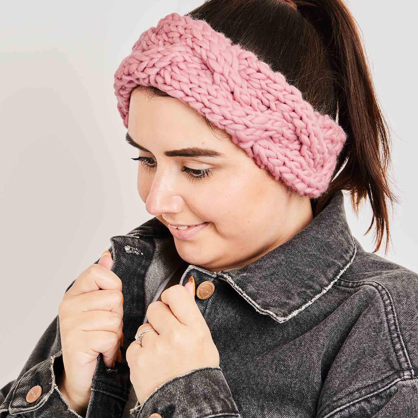 A woman is looking cosy wearing her Dust Pink Chunky Cable Headband, knitted from Stitch & Story's knitting kit using 100% super chunky merino wool.