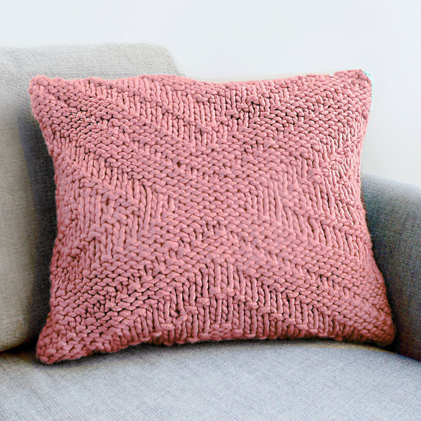 A Dust pink kingley cushion knitted from Stitch & Story knitting kit is sat on a grey sofa.