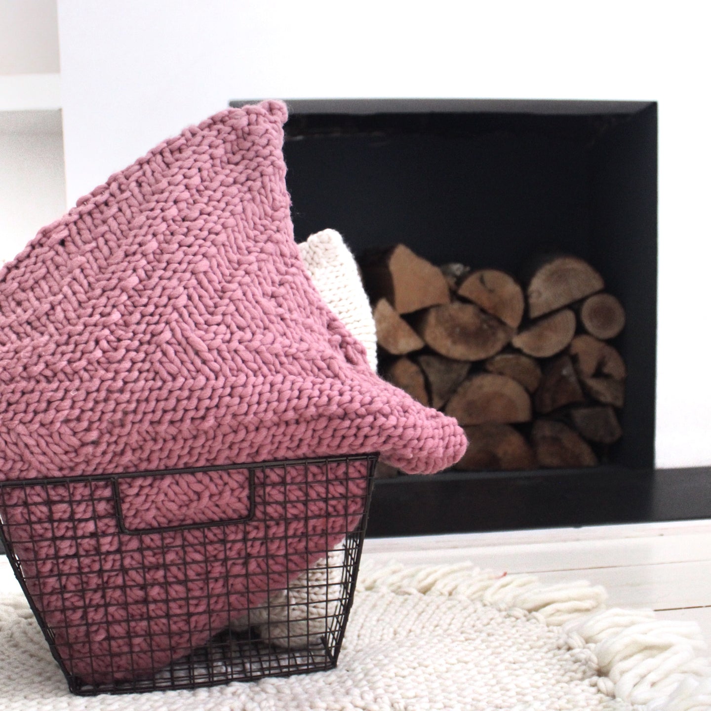 A Dust pink kingley cushion knitted from Stitch & Story knitting kit is placed in a homeware basket in front of a fire place