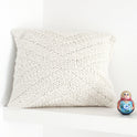 An Ivory White kingley cushion knitted from Stitch & Story knitting kit is placed on a grey sofa
