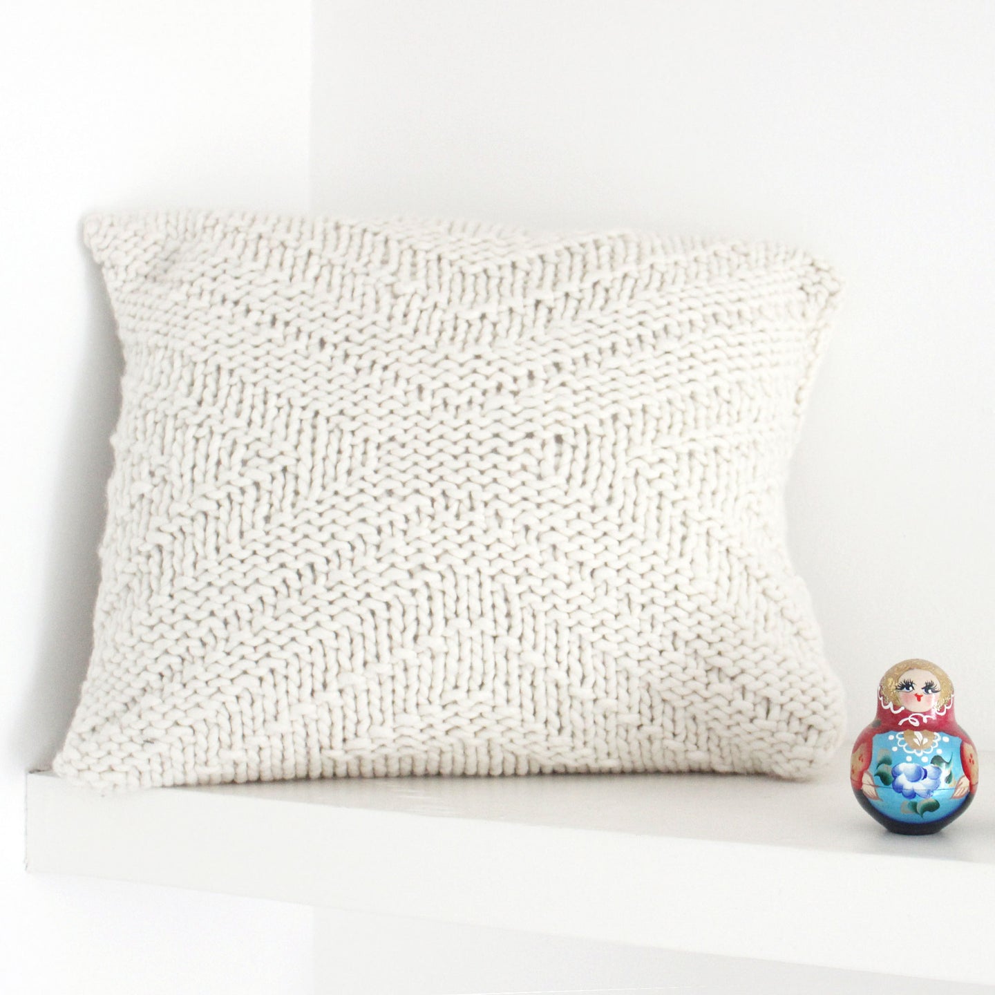 An Ivory White kingley cushion knitted from Stitch & Story knitting kit is placed on a grey sofa
