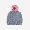 A Stitch & Story Luca Pom Hat in Stormy Grey with a dust pink pom pom, available as a starter knitting kit.
