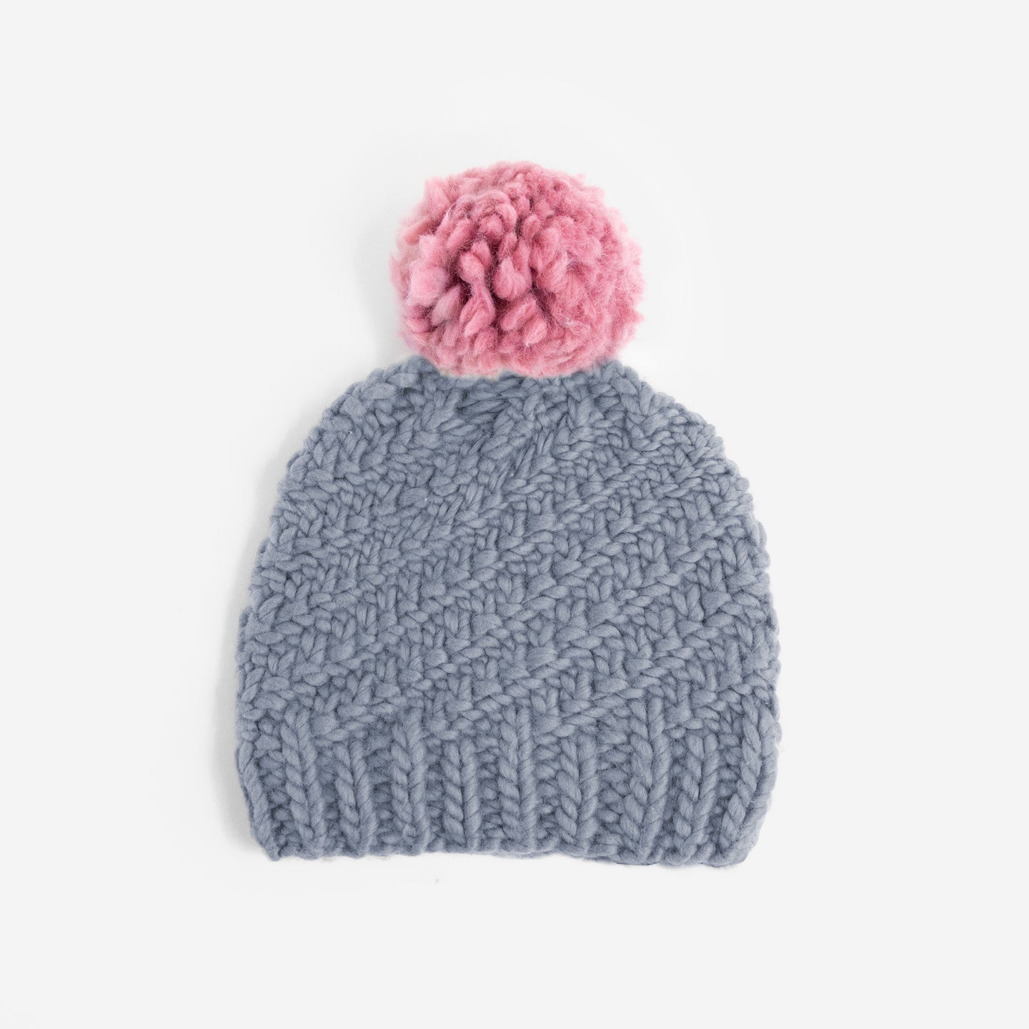 A Stitch & Story Luca Pom Hat in Stormy Grey with a dust pink pom pom, available as a starter knitting kit.