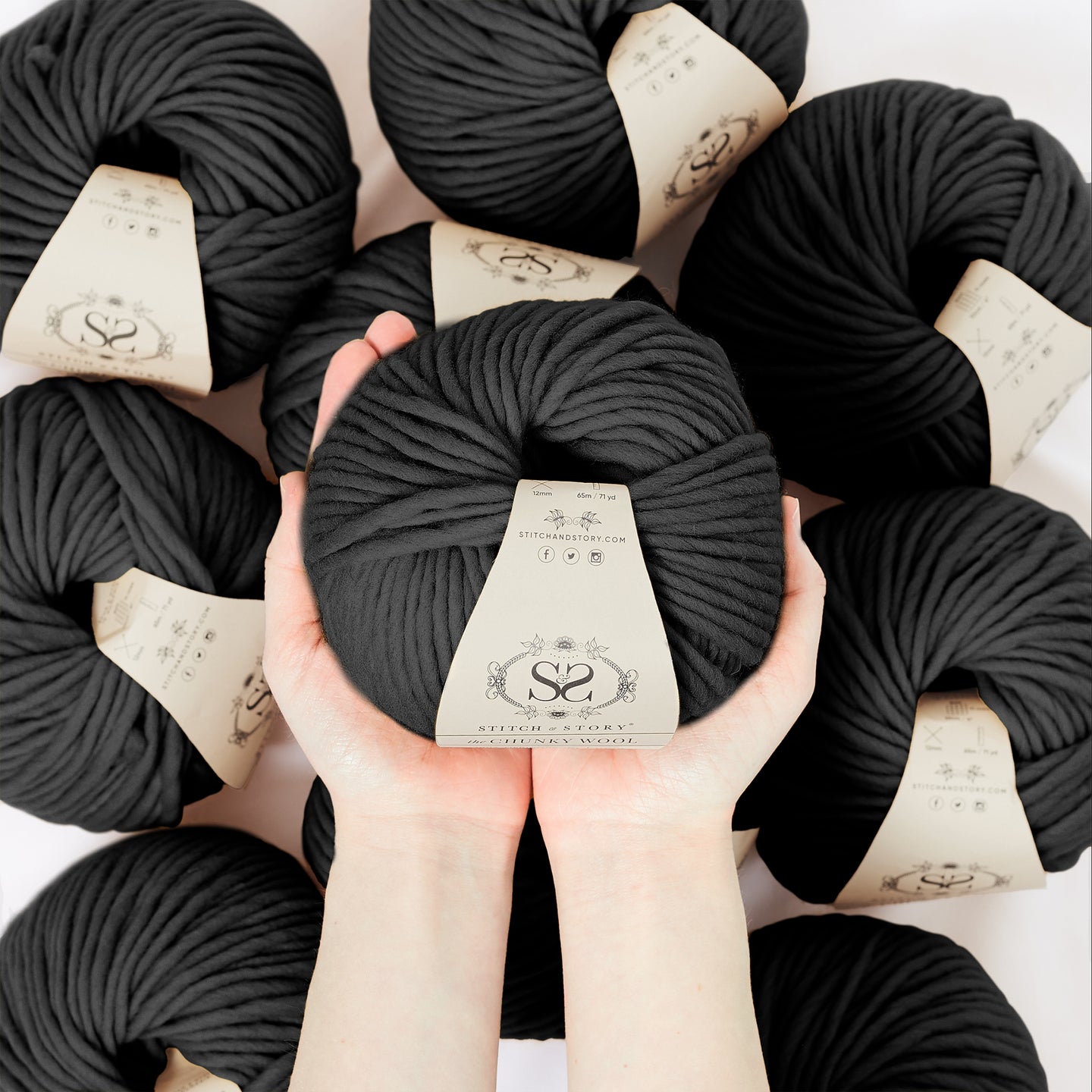 A hand is holding a ball of 100% merino wool Stitch & story The Chunky Wool in front of the camera, above another 9 balls of the same yarn. The colour shown here is star black