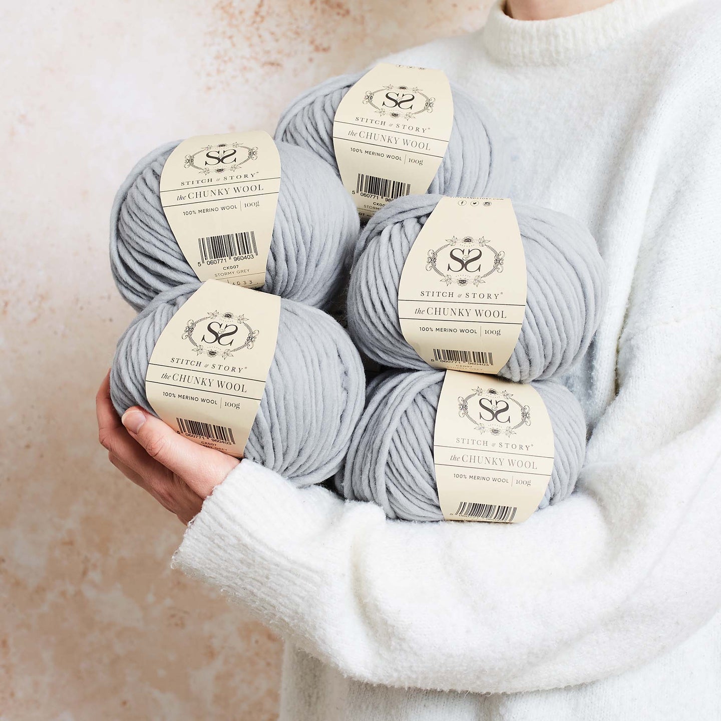 a person is holding 5 balls of Stormy Grey 100% merino wool The Chunky Wool from Stitch & story in a cosy manner, ready for a day of knitting.