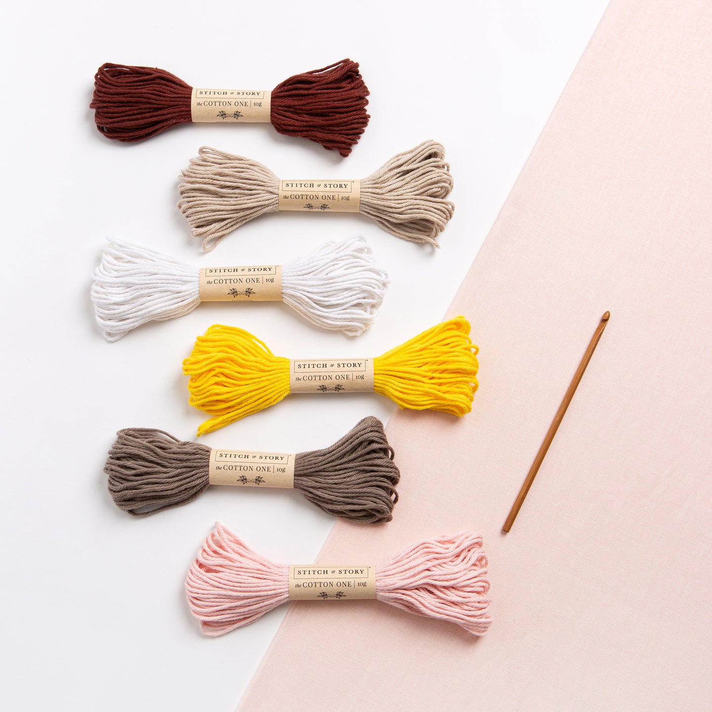 A stylised photo showing the 6 strands of 10g Cotton One yarn from Stitch & Story that you will receive with this kit, as well as a 4.5mm bamboo crochet hook.