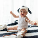 A very happy baby wearing a Snoopy beanie with flappy ears, and matching Snoopy baby booties, a knitting kit from Stitch & Story made with 100% merino wool.
