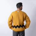 Showing the back of a man wearing a cosy fitted Charlie Brown sweater knitted from 100% merino wool The Chunky Wool from Stitch & Story. The sweater is in Mustard yellow with a graphic black chevron pattern at the bottom of the sweater. You can see the Peanut woven label at the back collar of the sweater.