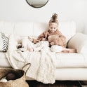 A pair of siblings are lying on the couch with the white Bounty Throw knitted from Stitch & Story knitting kit draped under them.