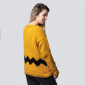 Showing the side profile of a woman  wearing a cosy fitted Charlie Brown sweater knitted from 100% merino wool The Chunky Wool from Stitch & Story. The sweater is in Mustard yellow with a graphic black chevron pattern at the bottom of the sweater.