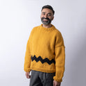 a man is wearing a cosy fitted Charlie Brown sweater knitted from 100% merino wool The Chunky Wool from Stitch & Story. The sweater is in Mustard yellow with a graphic black chevron pattern at the bottom of the sweater.