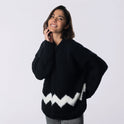 a woman is wearing a cosy fitted Charlie Brown sweater knitted from 100% merino wool The Chunky Wool from Stitch & Story. The sweater is in Star Black with a graphic White chevron pattern at the bottom of the sweater.