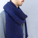 A man is looking cosy wearing his Midnight Blue Vale Scarf, knitted from Stitch & Story's knitting kit using 100% super chunky merino wool.
