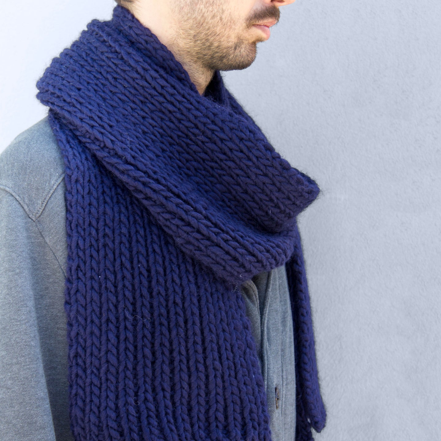 A man is looking cosy wearing his Midnight Blue Vale Scarf, knitted from Stitch & Story's knitting kit using 100% super chunky merino wool.