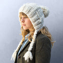A woman is wearing a newly knitted Cable Coo Hat in Ivory White, made from Stitch & Story's knitting kit.