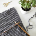 A work in progress photo showing a Fossil Grey mateusz snood being worked in the Stitch & story 100% merino Super chunky yarn with 12mm bamboo knitting needles.