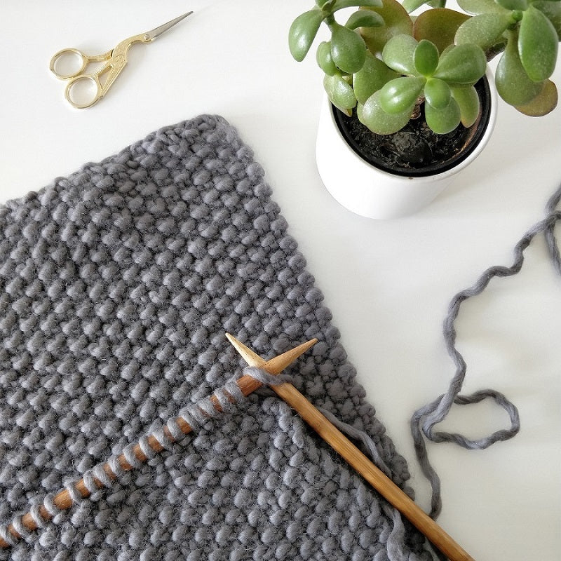 A work in progress photo showing a Fossil Grey mateusz snood being worked in the Stitch & story 100% merino Super chunky yarn with 12mm bamboo knitting needles.