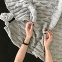 A pair of hand is softly draping the dove grey ivy geometric blanket knitting from a stitch & Story knitting kit.