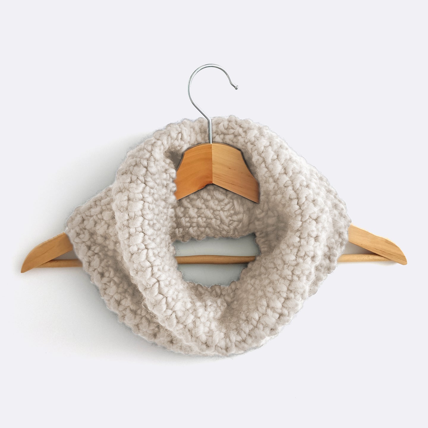 An Ivory White Mateusz Snood is hung on a hanger. This is knitted with the beginner friendly Stitch & Story knitting kit.