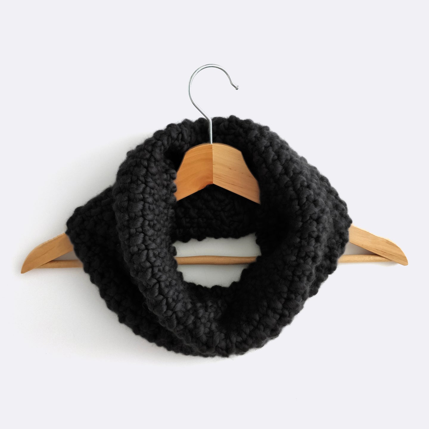 A Star Black Mateusz Snood is hung on a hanger. This is knitted with the beginner friendly Stitch & Story knitting kit.