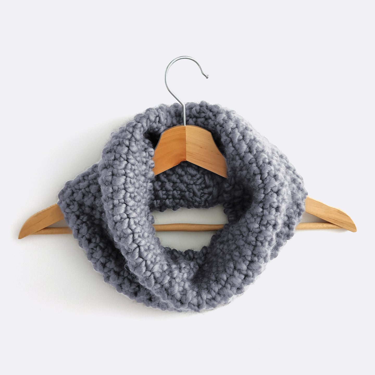 A Stormy grey Mateusz Snood is hung on a hanger. This is knitted with the beginner friendly Stitch & Story knitting kit.