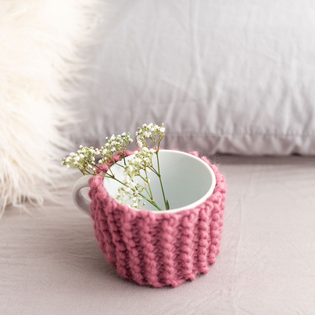 A pink cup cosy is used around a white mug.