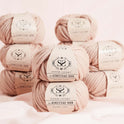 4 columns of 100% Super Chunky Homestead yarn by Stitch & story in Pink Peony are stacked on top of a soft pink silk, in front of the camera.