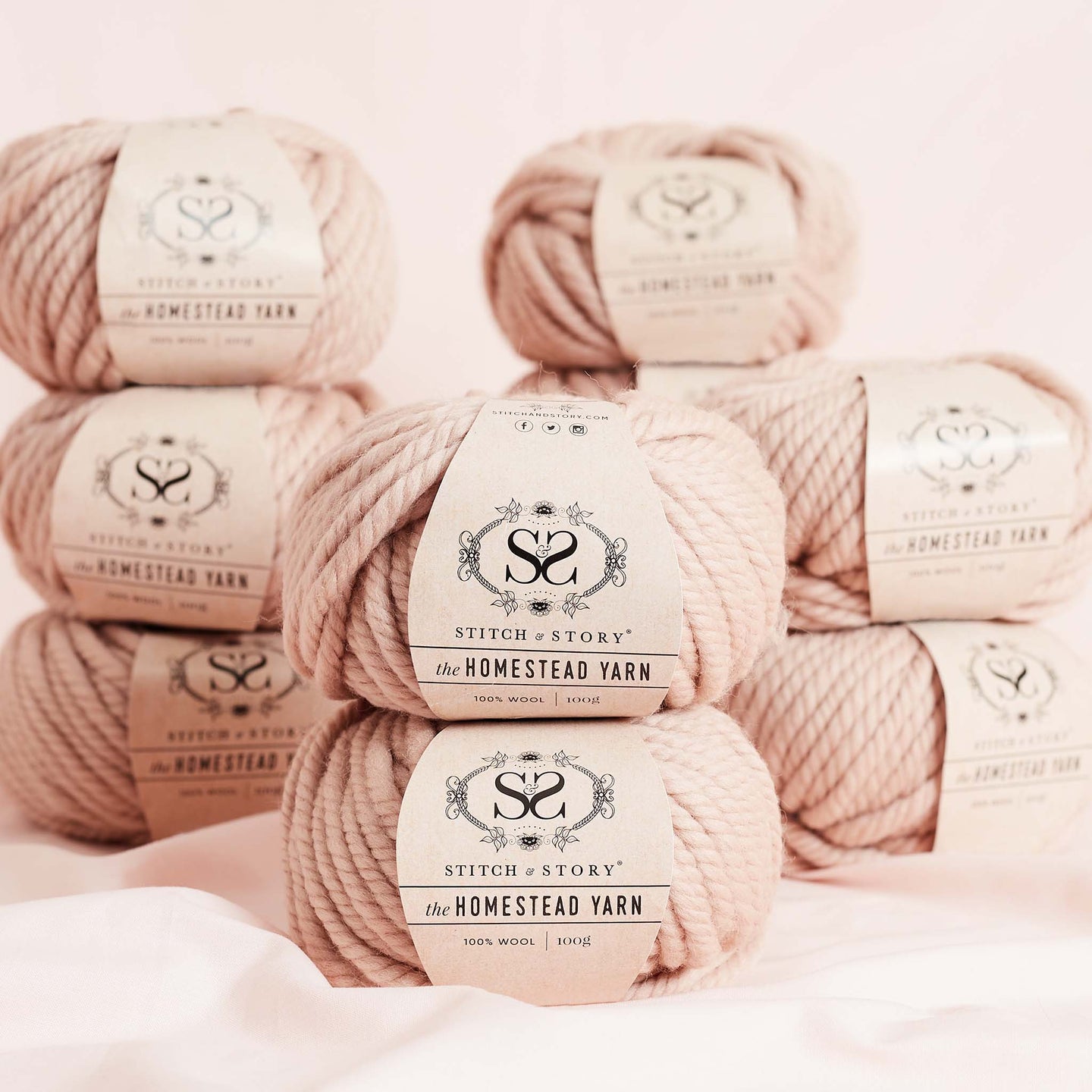 4 columns of 100% Super Chunky Homestead yarn by Stitch & story in Pink Peony are stacked on top of a soft pink silk, in front of the camera.