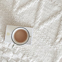 A white Bounty Throw is laid across the bed with a book and a cup of tea on top.