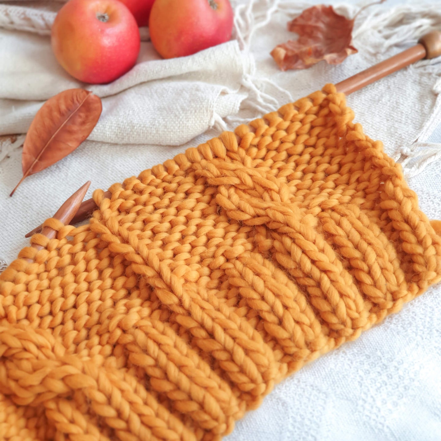 A work in progress photo showing a mustard yellow Cable Coo Hat is being knitted up with 12mm bamboo knitting needles, in Stitch & Story's 100% Merino The Chunky Wool