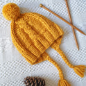 A mustard yellow Cable Coo Hat is knitted from the Stitch & Story Beginner friendly knitting kit.