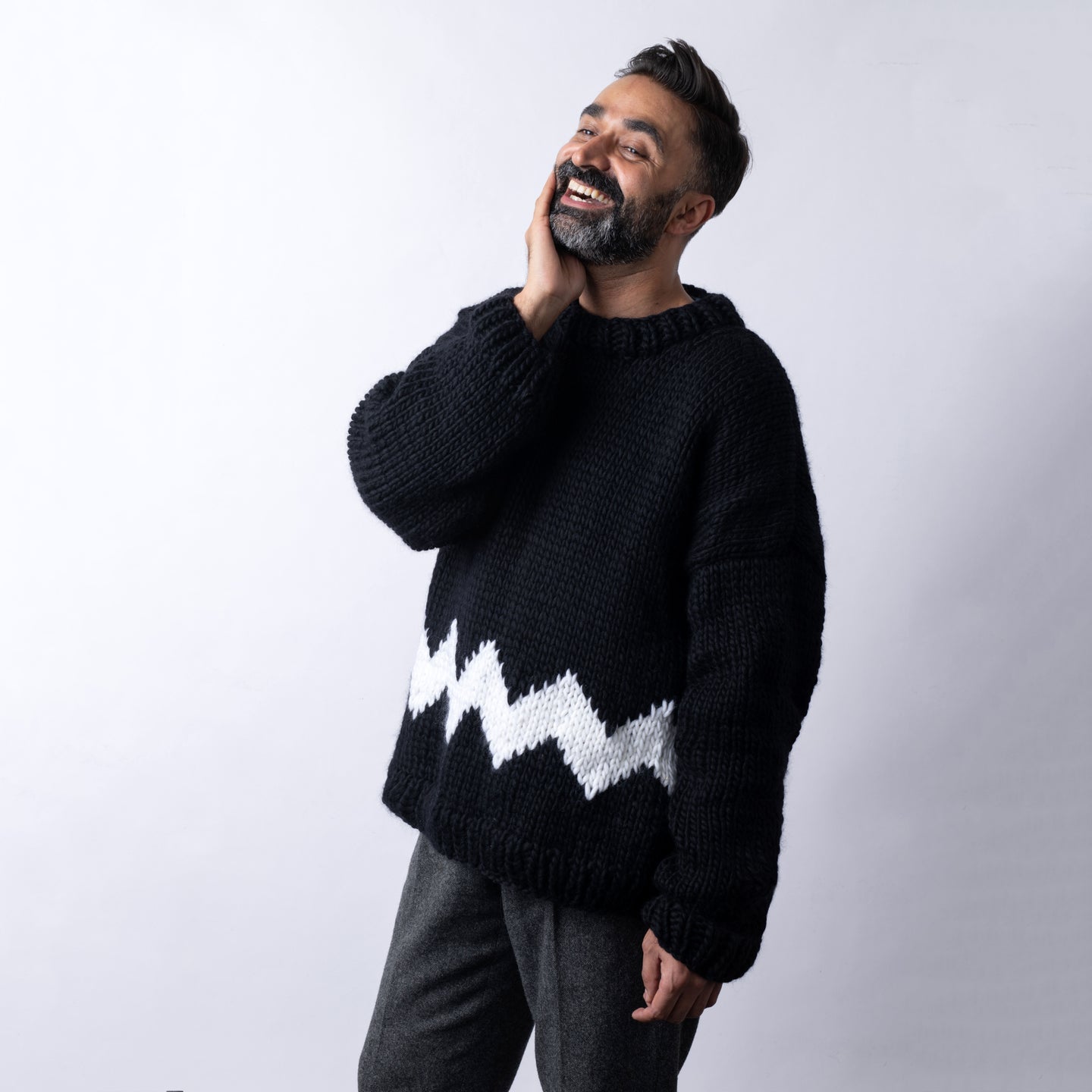 a man is wearing a cosy fitted Charlie Brown sweater knitted from 100% merino wool The Chunky Wool from Stitch & Story. The sweater is in Star Black with a graphic White chevron pattern at the bottom of the sweater.